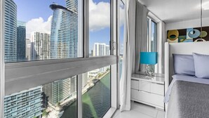 Ett modernt hotellrum med ett stort fönster som erbjuder utsikt över höga byggnader och en flod.