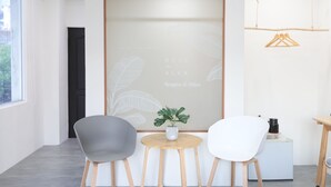A reception area with a modern design, featuring a reception desk, two chairs, a small table with a potted plant, and a wall with a leaf pattern and text. - EasyInn (Yuchi)