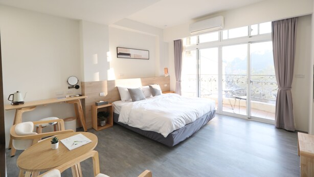 A modern hotel room with a bed, desk, chairs, and a balcony with a view. - EasyInn (Yuchi)