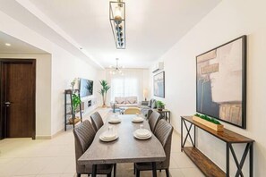 A modern dining area with a rectangular table set for four, surrounded by six upholstered chairs. A wooden console table with a plant is positioned to the right. - Mabaat - AL-Fayhaa - 514 (Jeddah)