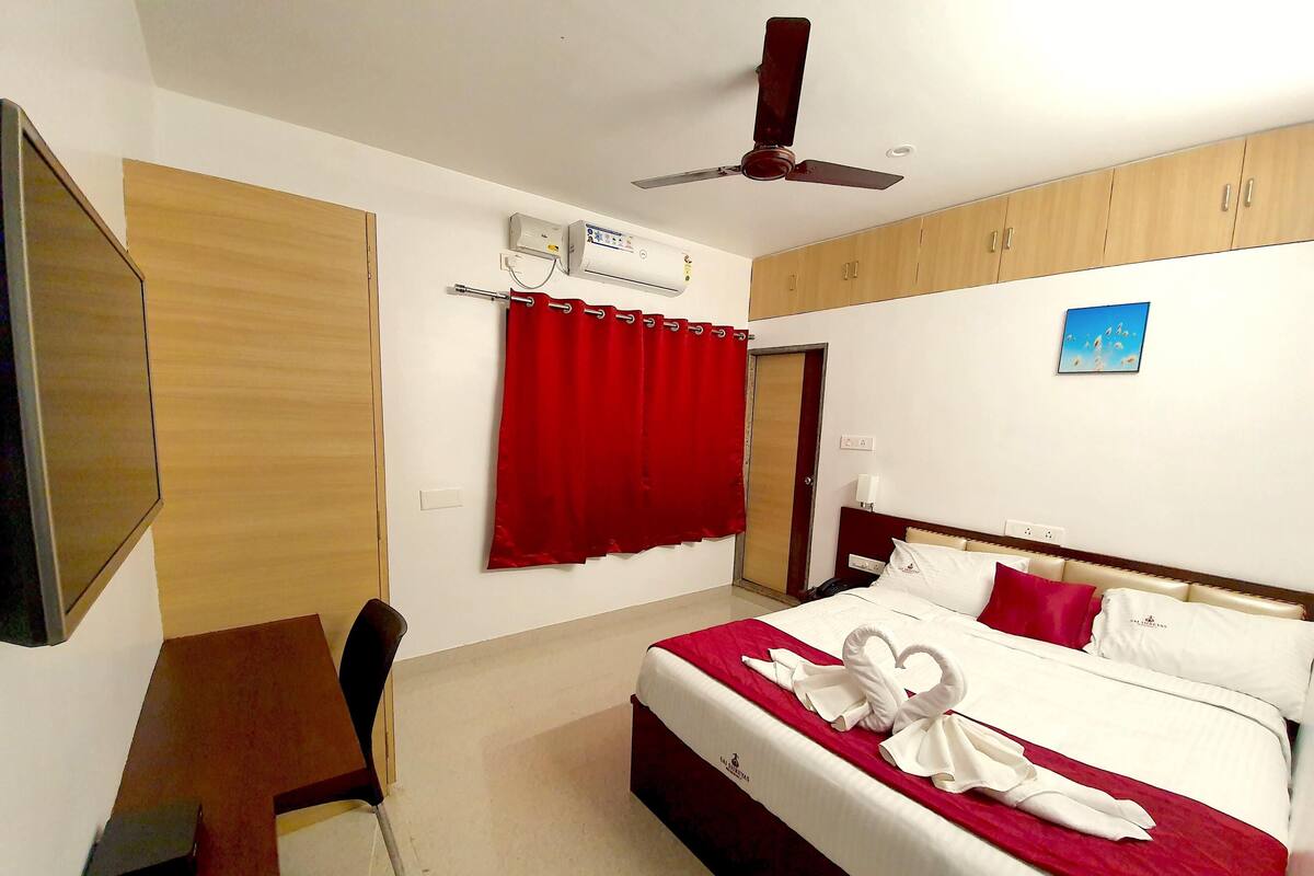 A hotel room with a bed, a desk, a chair, a ceiling fan, and a red curtain.