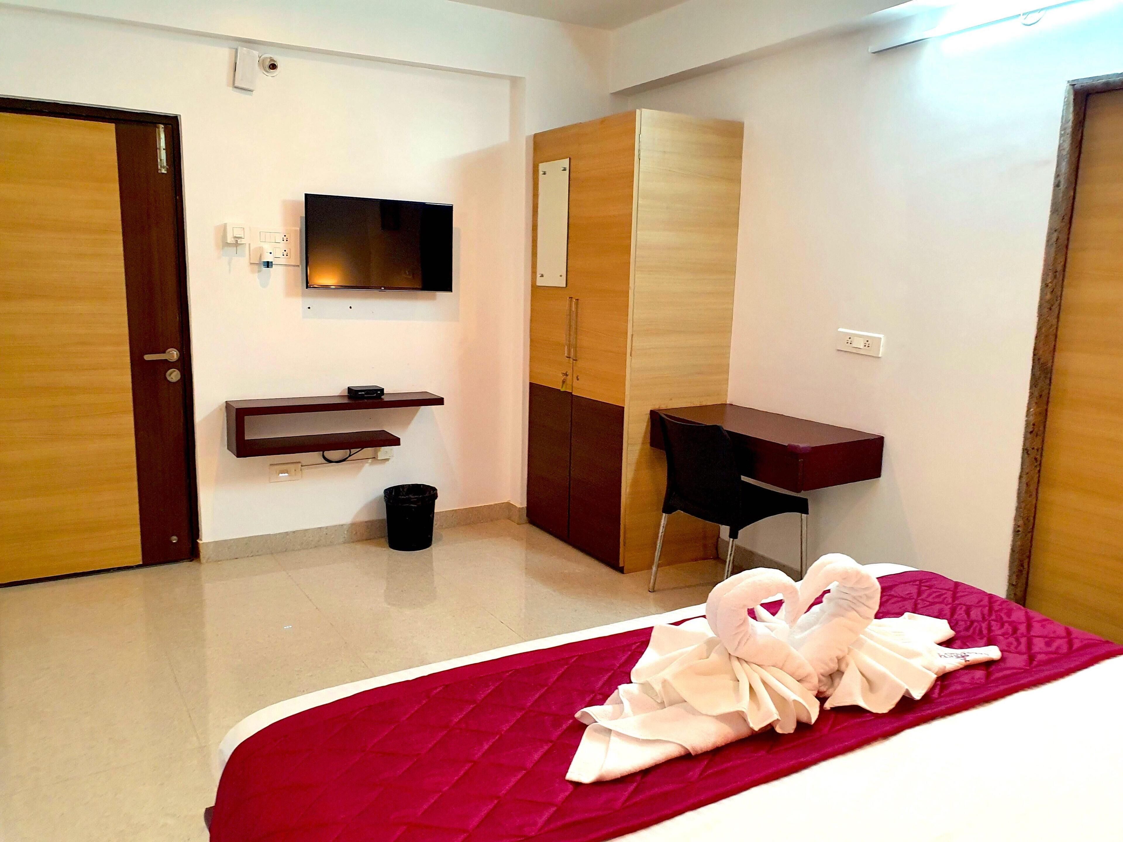 Una habitación de hotel con cama, escritorio, armario y televisor en la pared.