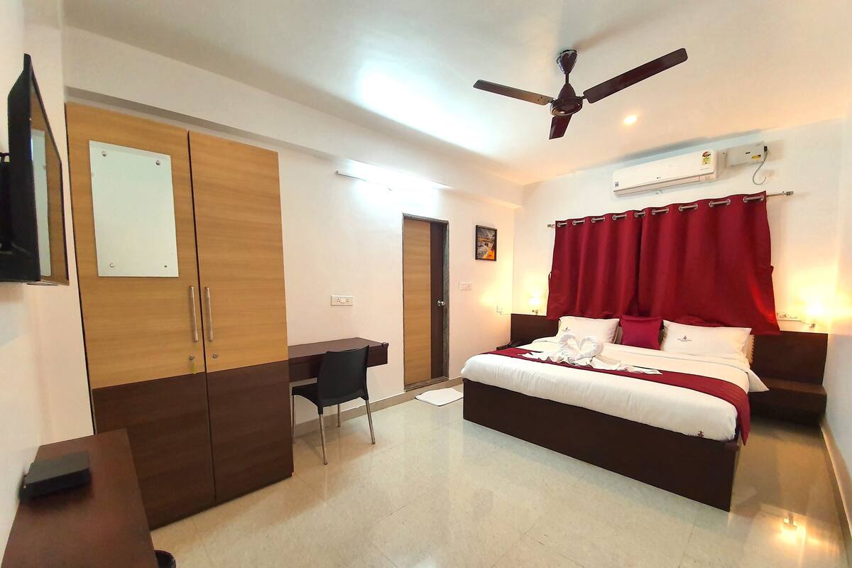 A hotel room with a bed, a desk, a wardrobe, a ceiling fan, and an air conditioning unit.