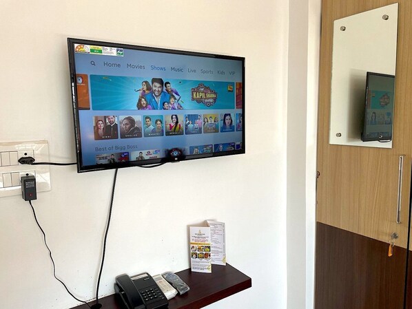 Une chambre d’hôtel équipée d’un téléviseur fixé au mur qui affiche l’interface d’un service de diffusion en continu, d’un téléphone et d’un présentoir à menus posé sur une étagère en bois.