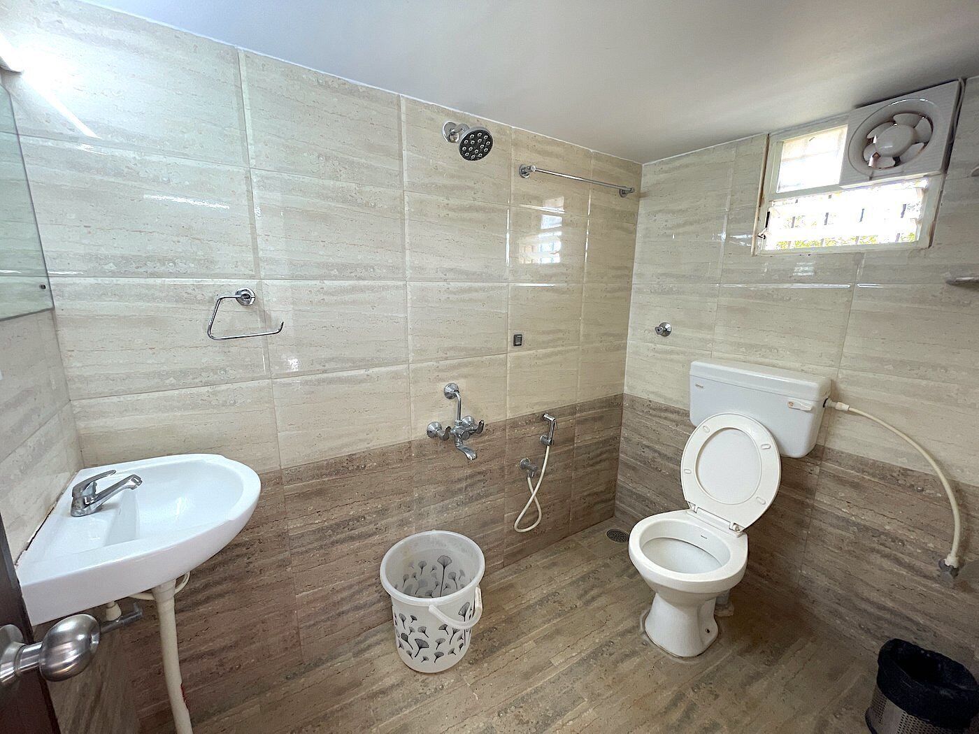 A bathroom with a sink, toilet, shower, and a small window.