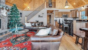 A spacious living area with a leather sofa, a Christmas tree, and a stone fireplace. - Spruce Cliffs at Timber Creek (Bethel)