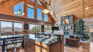 A spacious kitchen with a large island, wooden cabinetry, and a stone fireplace. - Spruce Cliffs at Timber Creek (Bethel)