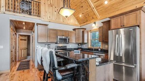 A spacious kitchen with wooden cabinets, a stainless steel refrigerator, and a large island with bar stools. - Spruce Cliffs at Timber Creek (Bethel)