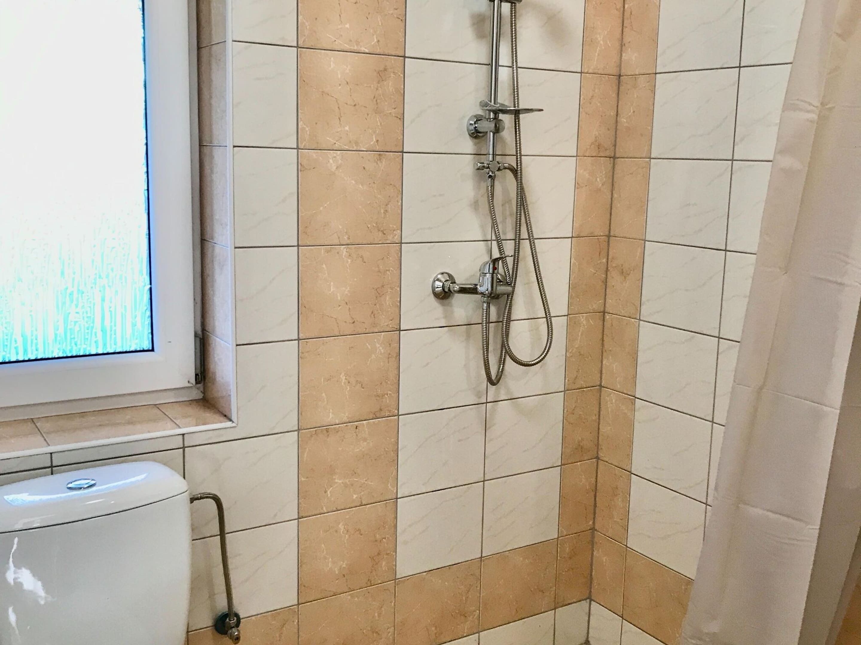 Ein Badezimmer mit Dusche, Toilette und Fenster.