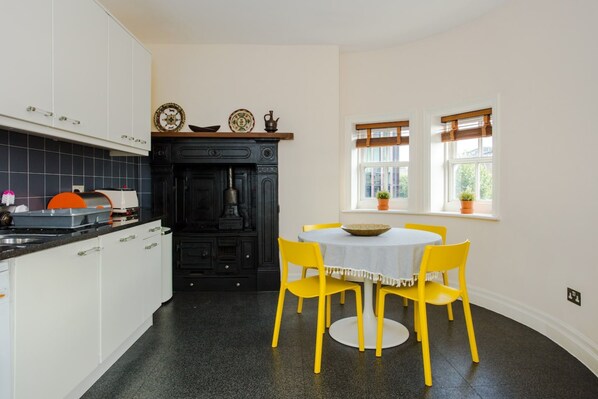 A kitchen with white cabinets, a black stove, and a dining table with yellow chairs. - Luxury 2 Bedroom Apartment in London Bridge (London)
