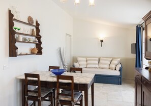 Un coin repas avec une table en marbre et des chaises en bois, un canapé avec des coussins à rayures et une étagère murale agrémentée d’objets décoratifs.