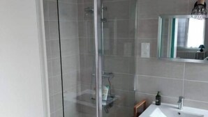 Une salle de bain moderne avec une douche à parois de verre, un lavabo blanc et un miroir au-dessus.