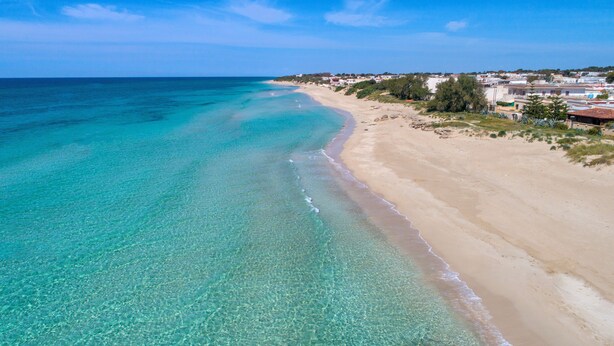 Une plage côtière aux eaux turquoise et limpides, bordée d’un rivage sablonneux.