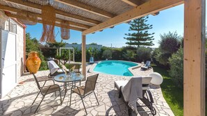Une terrasse extérieure avec une piscine, un sol en pierre et une pergola en bois.