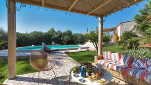 Un espace extérieur abrité comprenant une piscine, un sol en pierre, des meubles en osier et une table garnie de nourriture et de boissons.