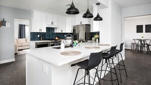 Una cocina moderna con armarios blancos, una isla grande con taburetes de bar e iluminación colgante.