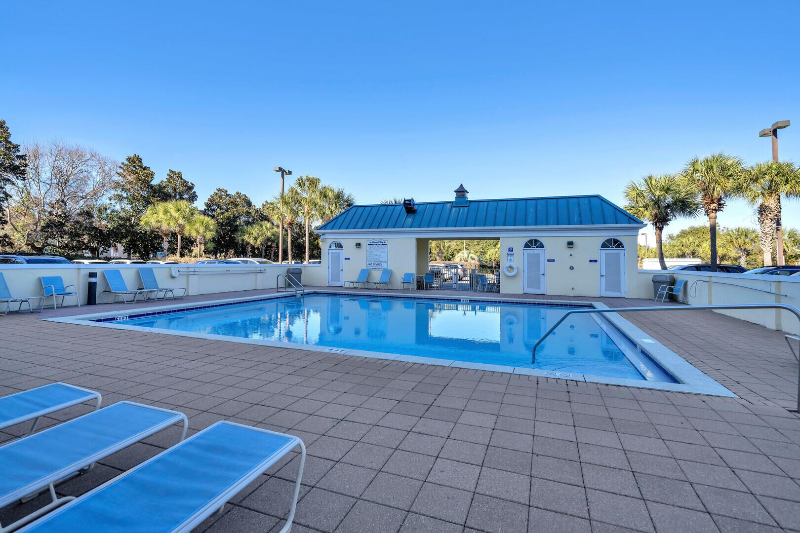 En swimmingpool med liggestole, et overdækket område og en bygning med et blåt tag.
