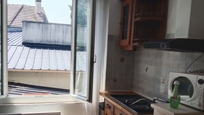 A kitchen with a window, wooden cabinets, a microwave, and a sink. - Andrea apartment (Fontenay-sous-Bois)