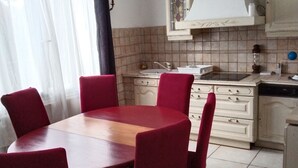 A dining area with a round table and six red chairs, a kitchen with white cabinets, and a window with sheer curtains. - Andrea apartment (Fontenay-sous-Bois)