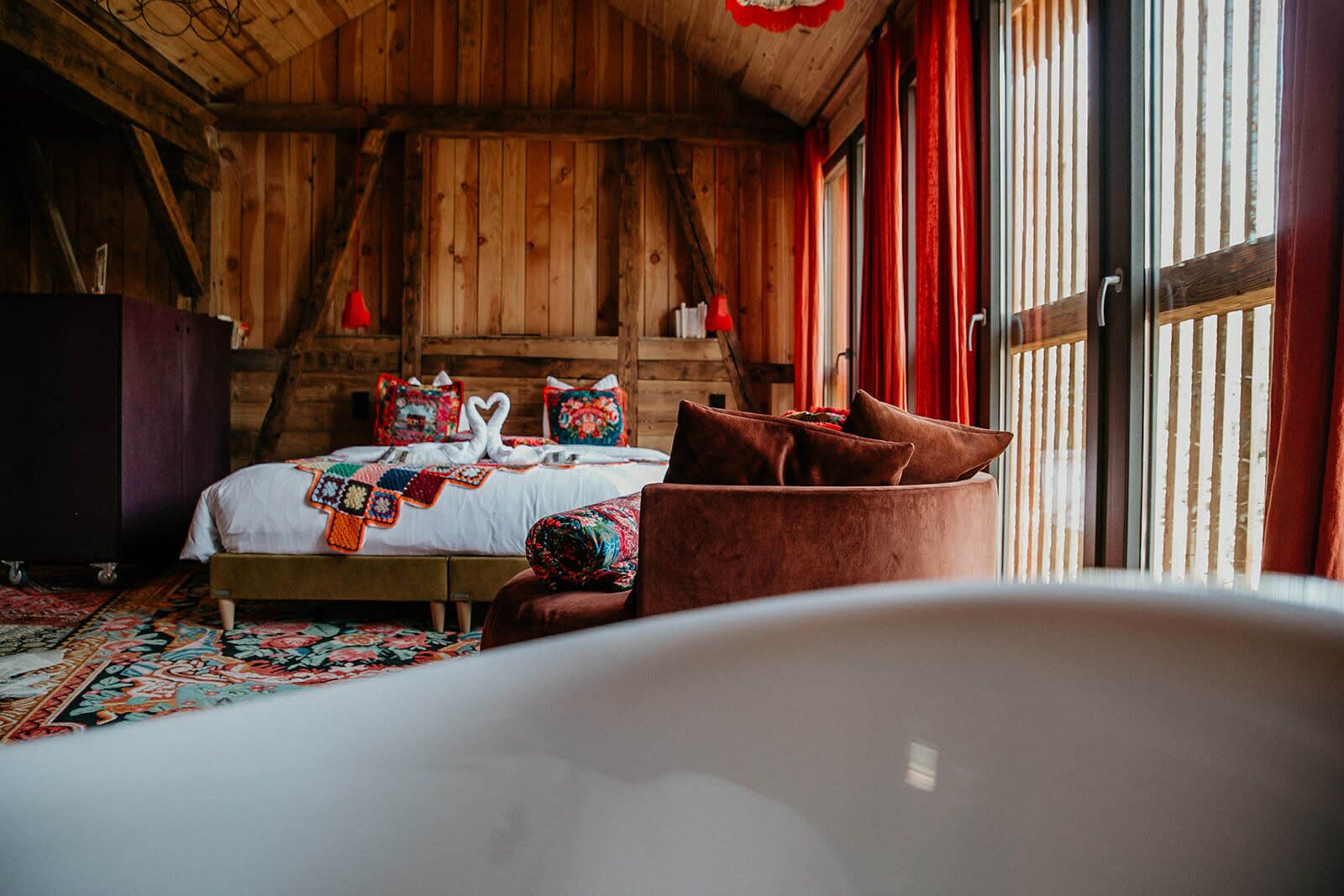 A wooden cabin-style bedroom with a bed, pillows, and a red curtain.