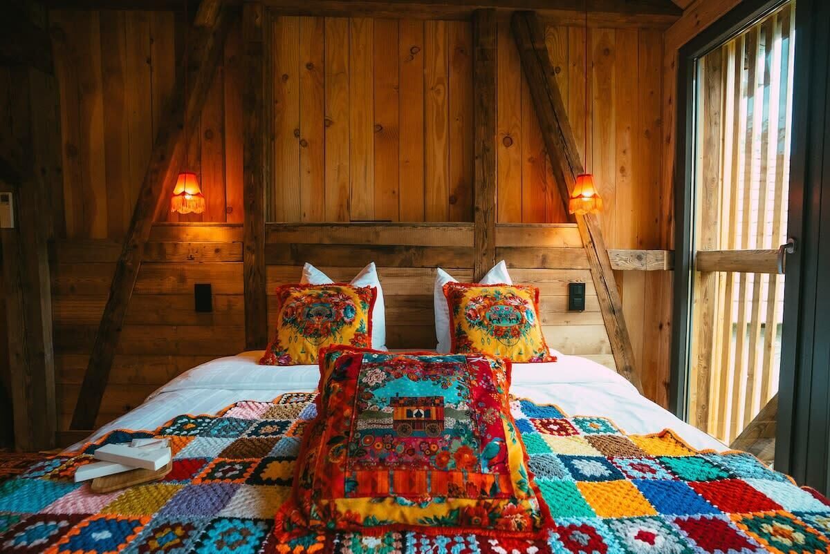 Ein gemütliches Zimmer mit Holzwänden, einem großen Bett mit bunten Quilts und zwei Wandleuchten.