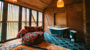 A rustic bathroom with a bathtub, wooden walls, and a large window. - "La Bohème" Chic & Unique Designer Loft in Alsace (Guebwiller)