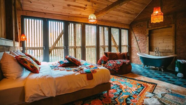 A wooden cabin bedroom with a large bed, a bathtub, and a colorful rug. - "La Bohème" Chic & Unique Designer Loft in Alsace (Guebwiller)