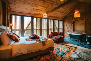 Un dormitorio de cabaña de madera con una cama grande, una bañera y una alfombra colorida.