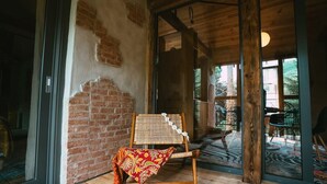 A room with a wooden floor, a wicker chair, and a glass door leading to an outdoor area with a patterned rug.