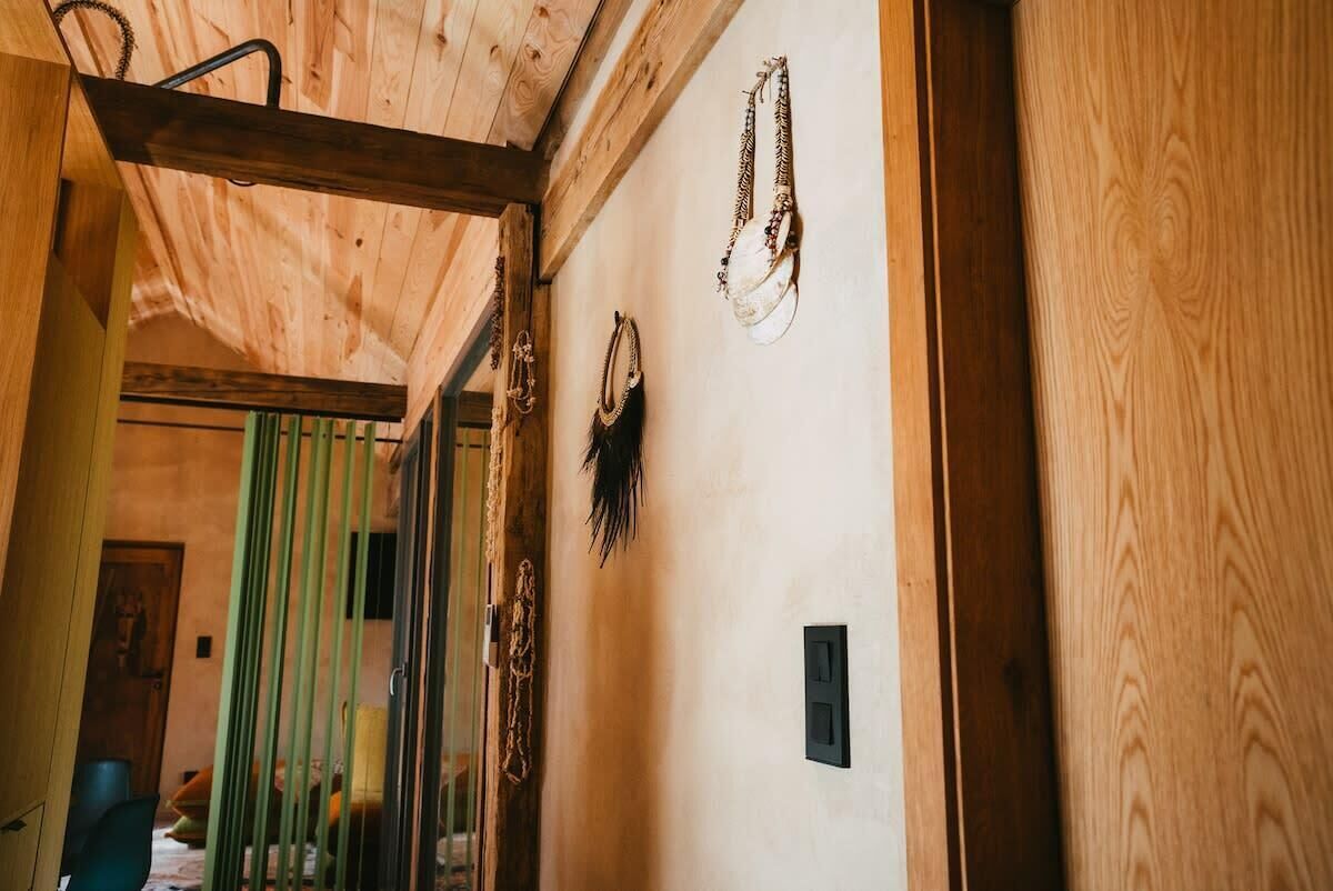 A wooden interior with a ceiling beam, a wall-mounted light switch, and a door with a green curtain.