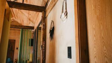 A wooden interior with a ceiling beam, a wall-mounted light switch, and a door with a green curtain.