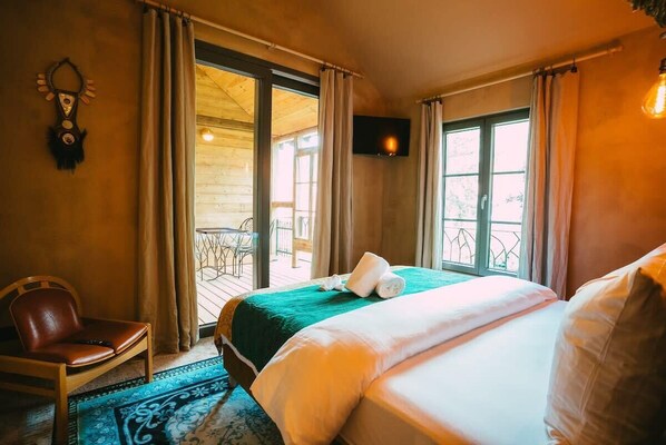 Habitación de hotel con cama, una silla, televisión y balcón con mesa y sillas.