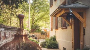 Une cour avec une fontaine rustique, un bâtiment en bois doté d’une porte, et une végétation luxuriante.
