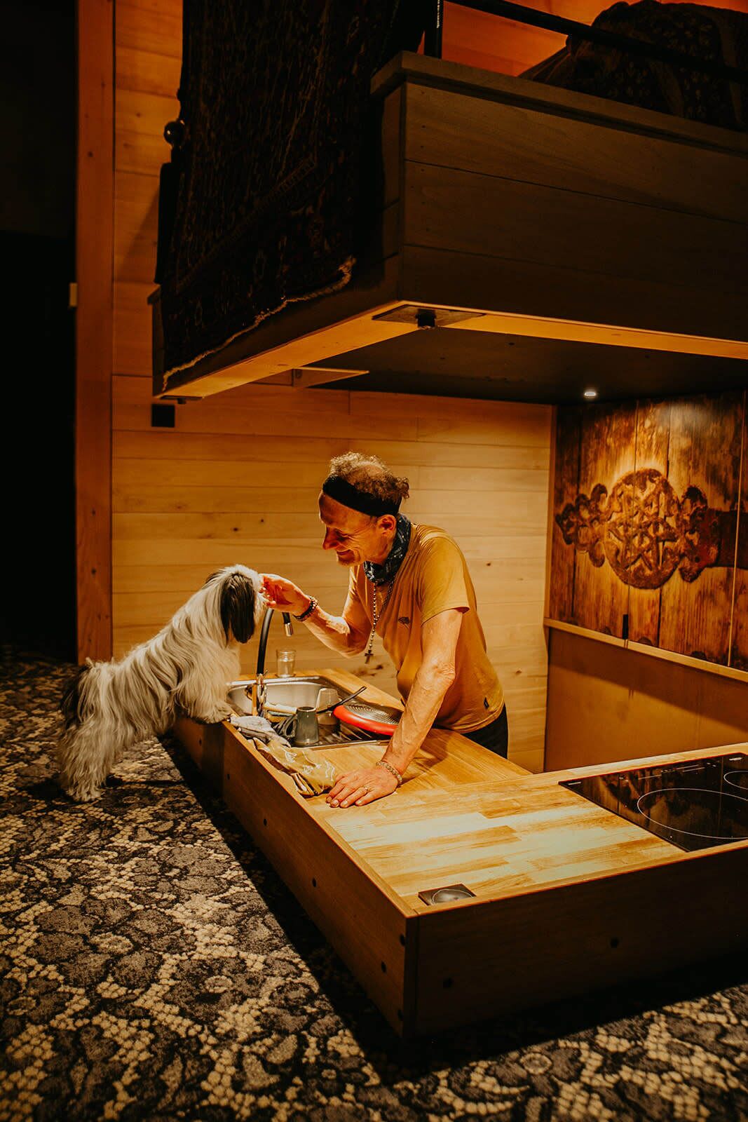 A wooden bunk bed with a lower bunk, a wooden table, and a patterned carpet.
