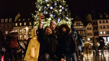 En grupp människor som tar en selfie framför ett julpyntat julgran på ett torg i en stad.