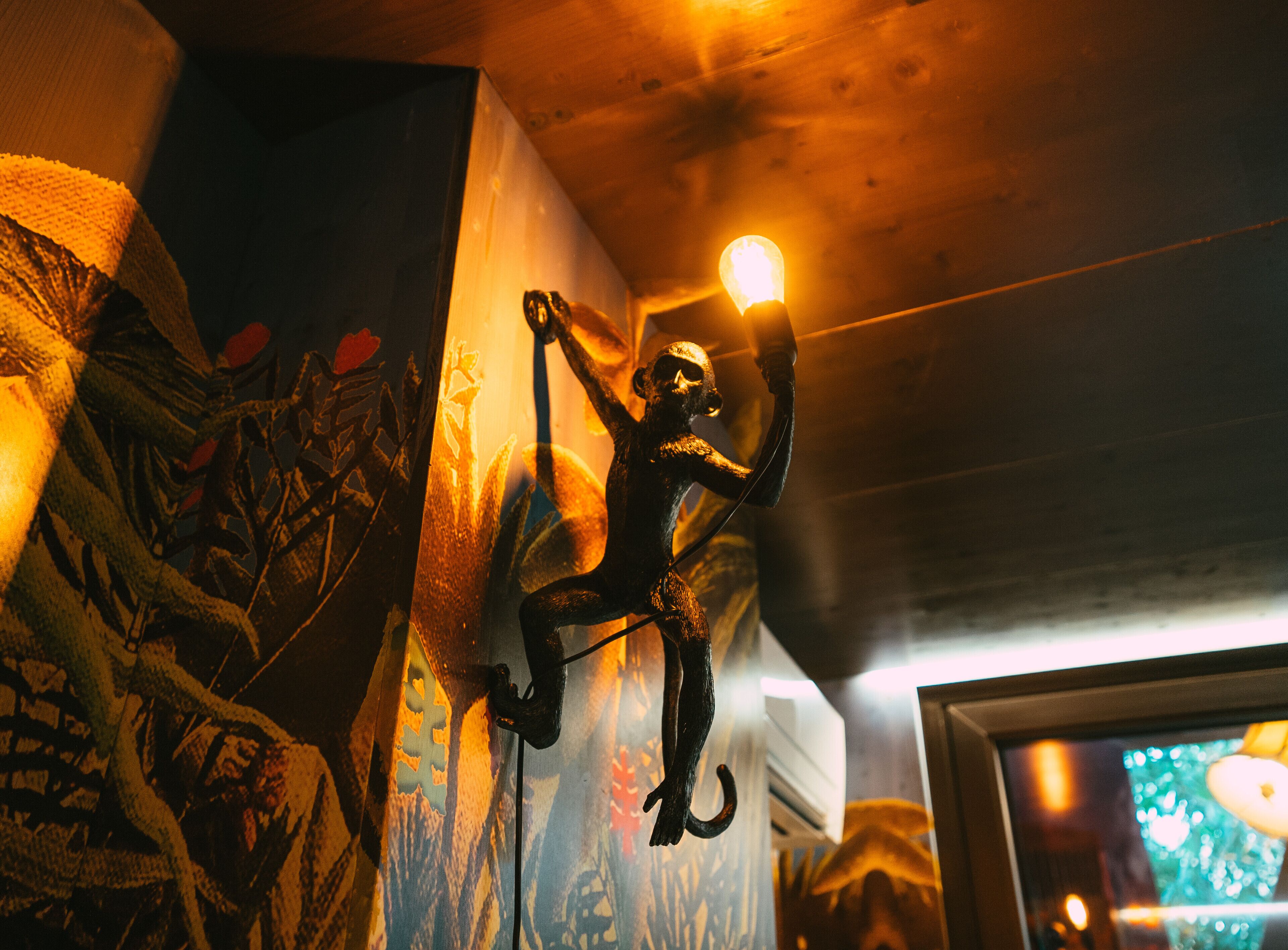 Une pièce ornée d’une fresque murale, d’un luminaire suspendu et dont l’encadrement de porte est visible.