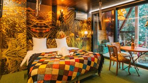 Ein Zimmer mit einem großen Bett, einem kleinen Tisch mit Stühlen und Blick auf Grün.