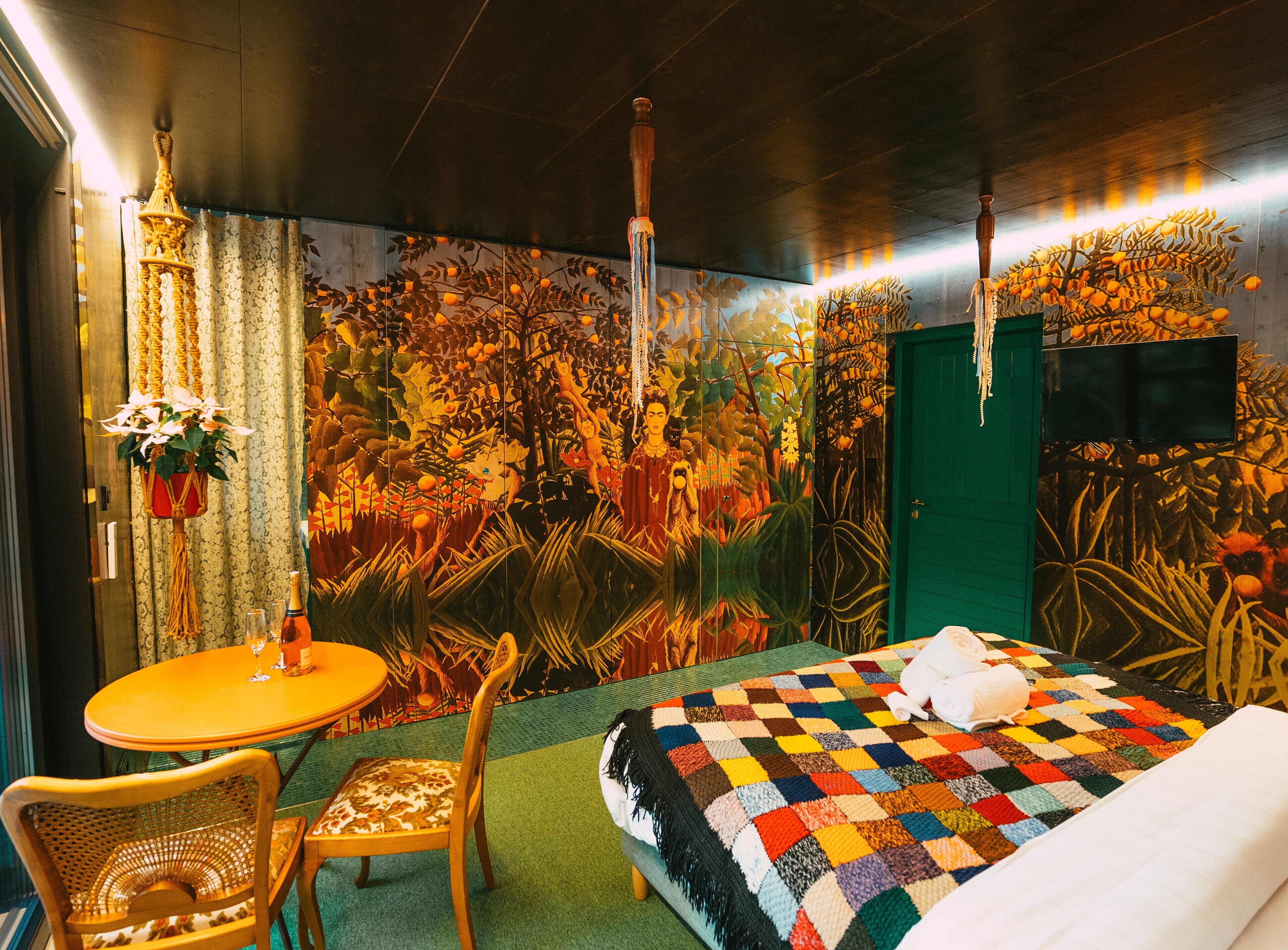 Een kamer met een bed, een ronde tafel, een stoel, een groene deur en een muur met een muurschildering.