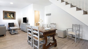 Ein Essbereich mit Holztisch, weißen Stühlen, einem Fernseher und einer Treppe.