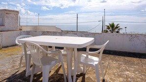 Een witte plastic tafel en stoelen op een terras op een dak, met uitzicht op zee.