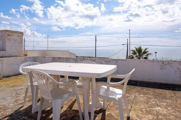 A white plastic table and chairs on a rooftop terrace with a view of the sea.
