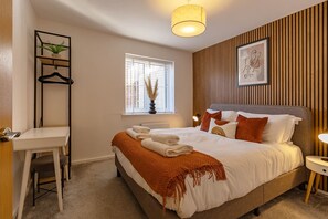 Une chambre bien rangée, avec un lit, une table de chevet et une fenêtre équipée de stores.
