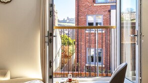 A bedroom with a bed, a chair, a window with a view of a brick building, and a clock on the wall.