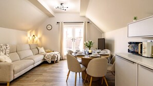 A modern living room with a sofa, dining table, chairs, and a kitchen area with a microwave.