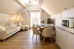 A modern living room with a sofa, dining table, chairs, and a kitchen area with a microwave. - Curlew House, with parking and Abbey views! (North Yorkshire)