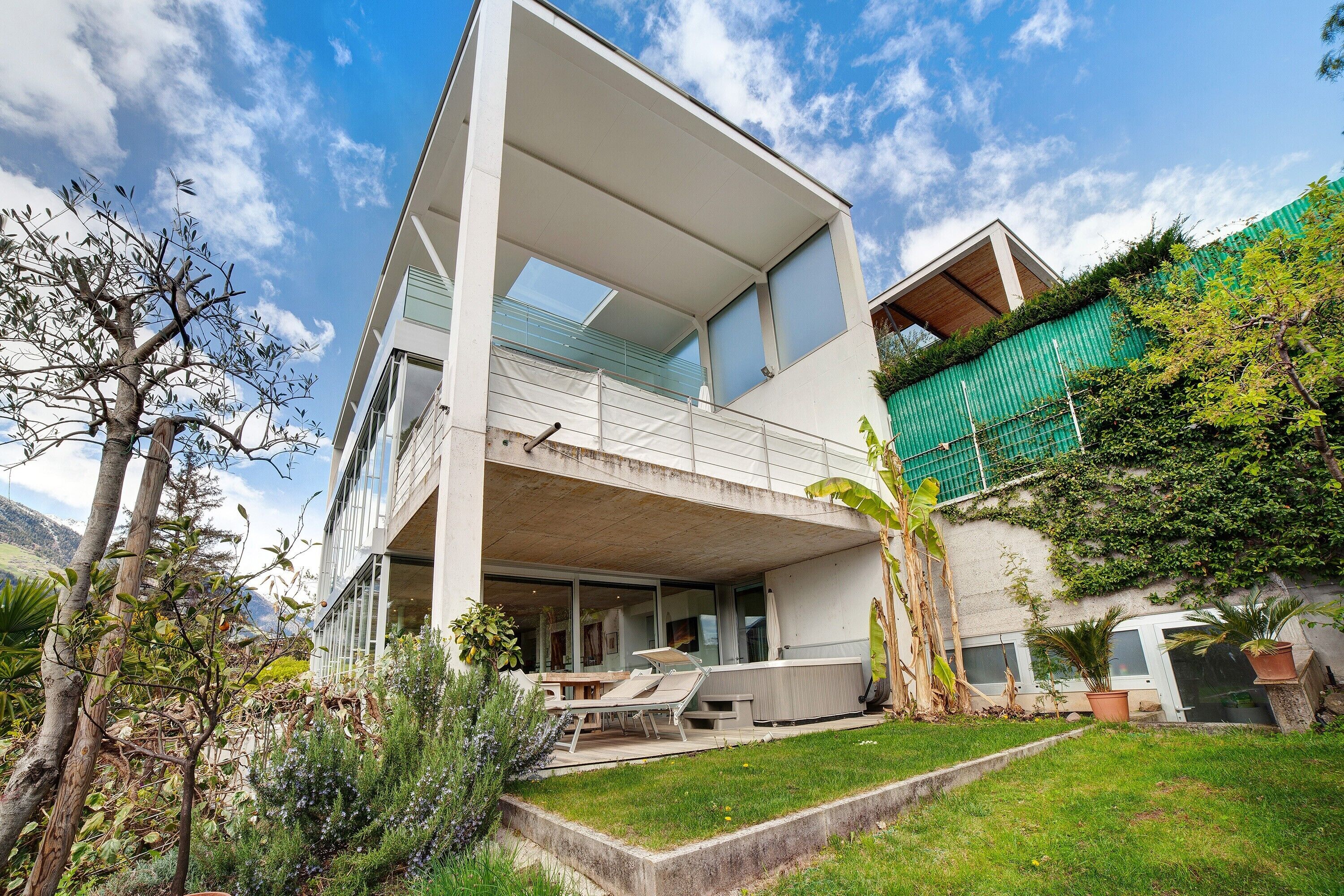 A modern two-story house with a balcony, outdoor seating, and a hot tub.