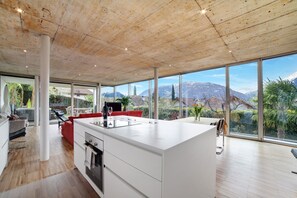 Een moderne keuken met een groot eiland, een eethoek met rode stoelen en grote ramen met uitzicht op bergen.