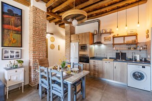 Cozinha moderna com parede de tijolos, vigas de madeira no teto e área de refeições com mesa e cadeiras.
