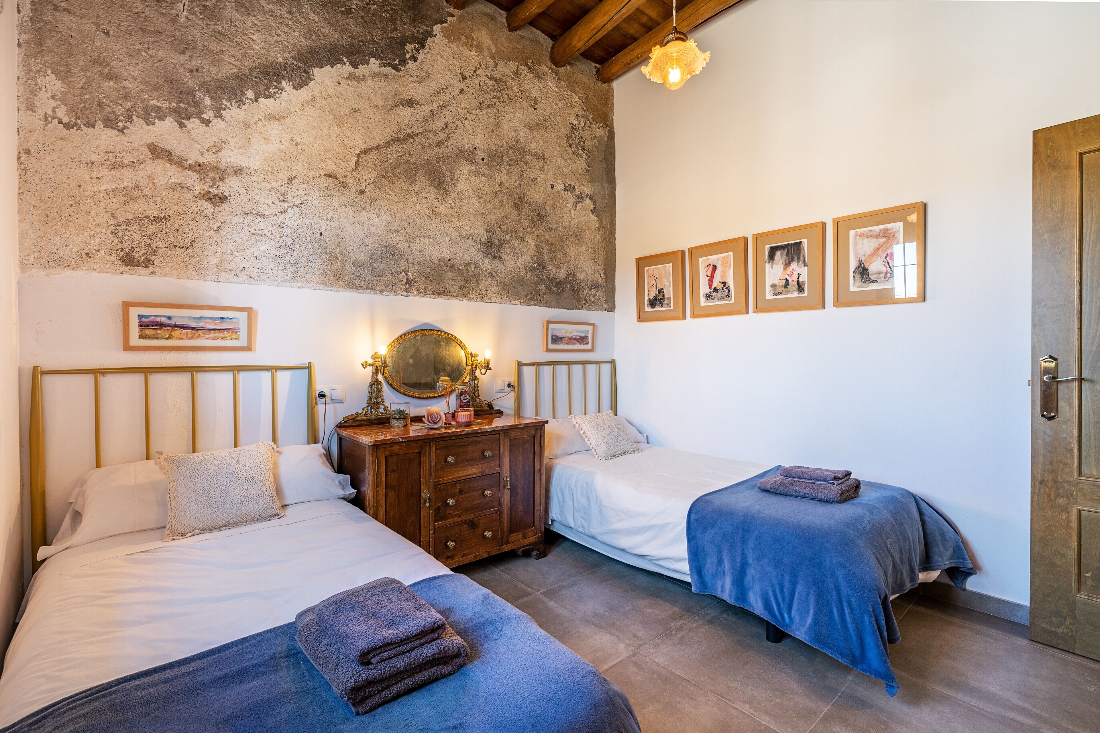 A room with two beds, a wooden dresser, a mirror, and framed pictures on the wall.