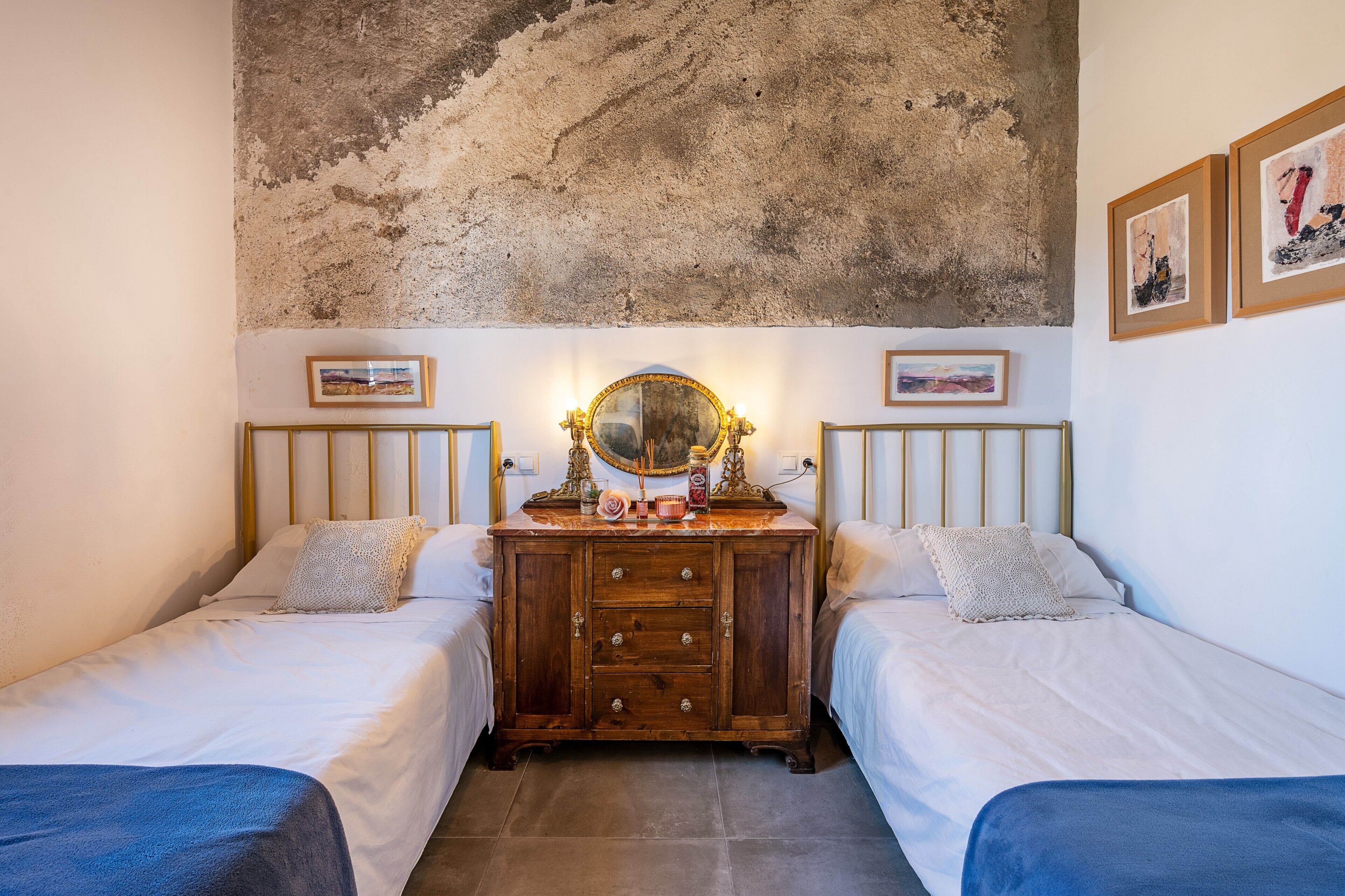 Une chambre avec deux lits, une commode en bois, un miroir et des œuvres d’art accrochées aux murs.